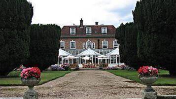 A large, two-story building with a symmetrical facade, a covered outdoor area with white canopies, and a gravel pathway leading to the entrance.