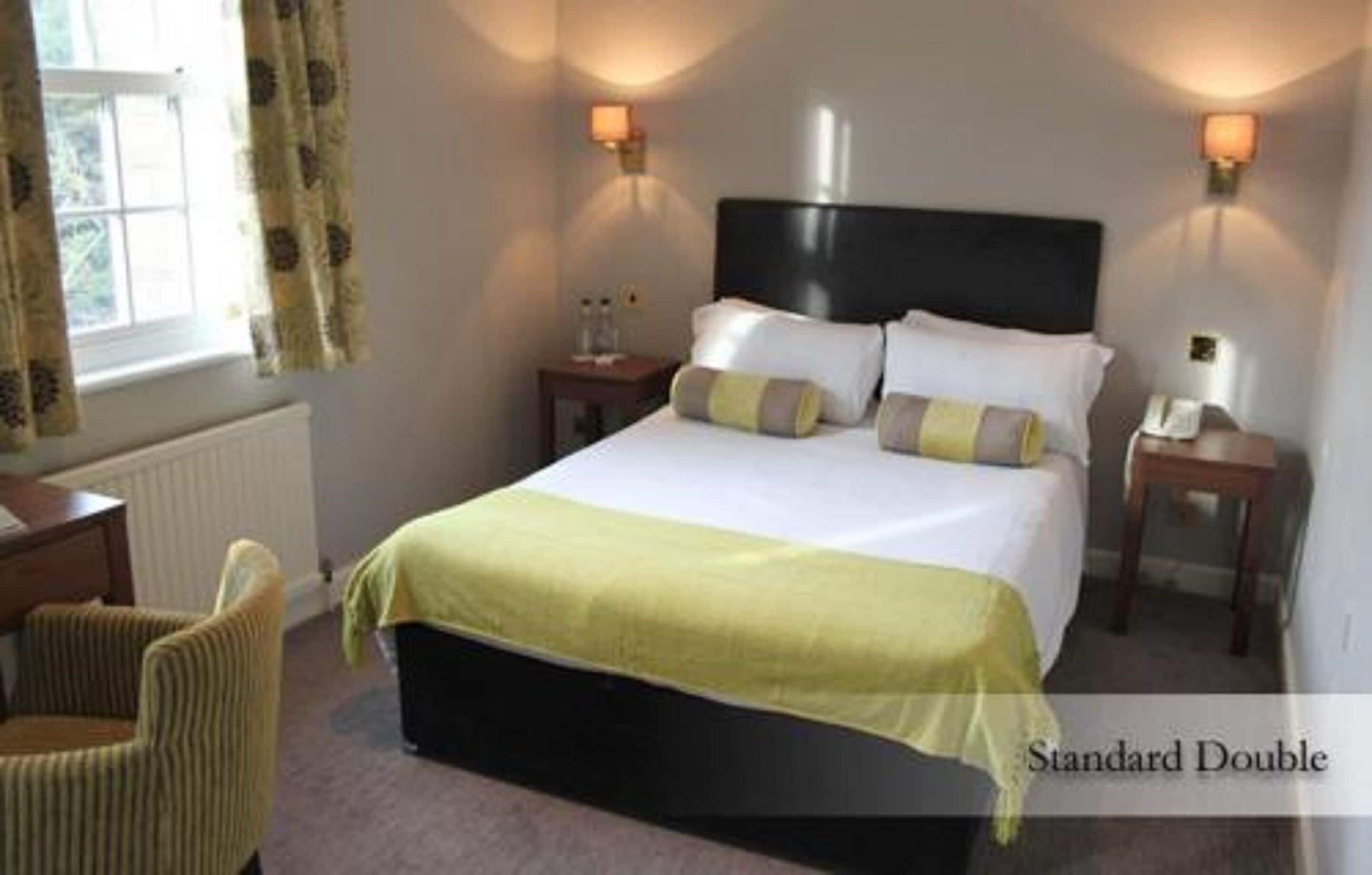 A standard double room with a bed, two bedside tables, a chair, and a window with curtains.