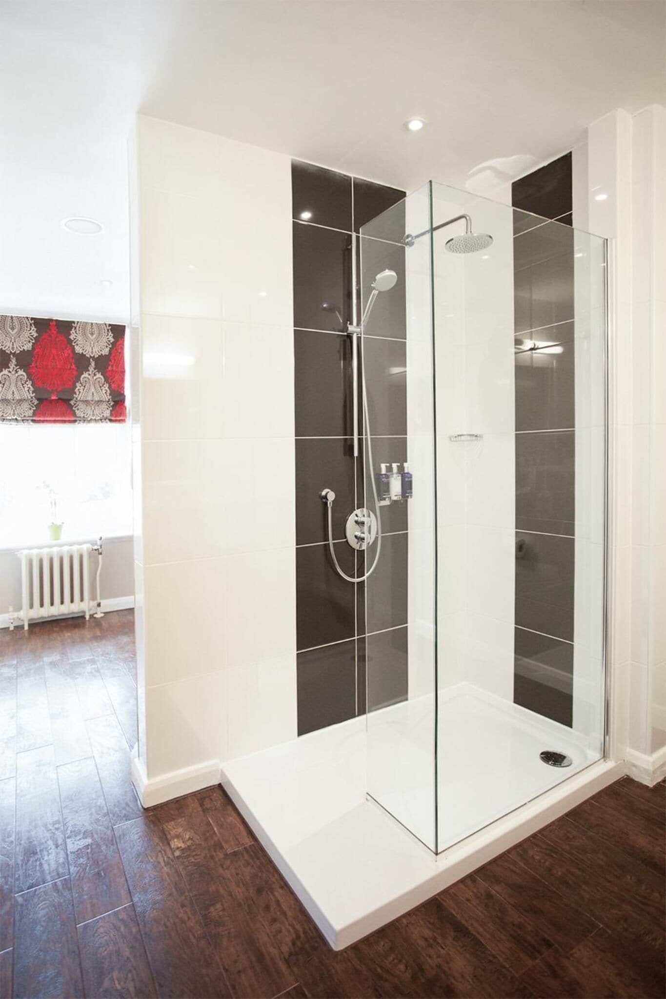 A modern bathroom with a glass-enclosed shower, white tiles, and a wooden floor.