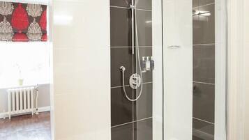 A modern bathroom with a glass-enclosed shower, white tiles, and a wooden floor.
