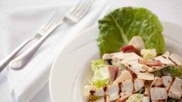 Prato de salada de frango grelhado com alface e bacon, acompanhado de um garfo e guardanapo sobre uma toalha de mesa branca.