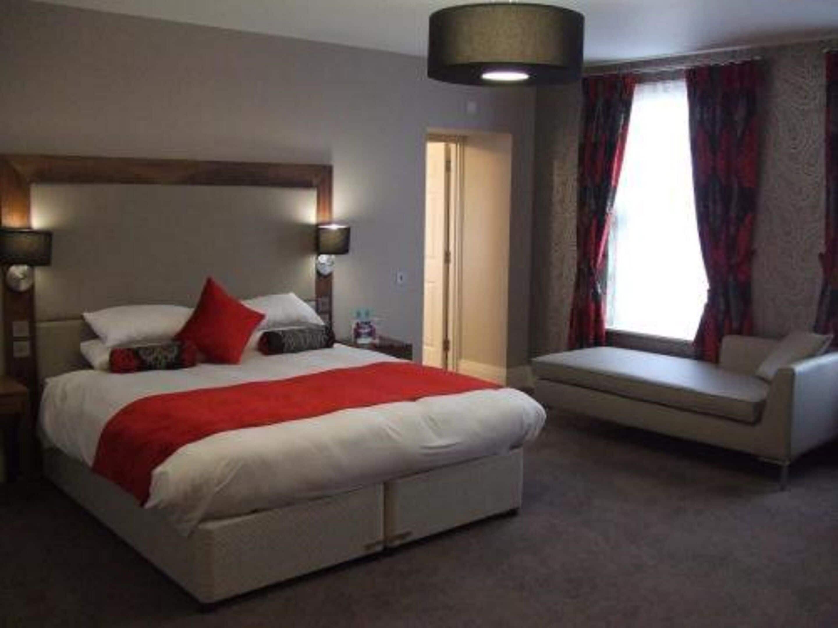 A bedroom with a large bed, bedside lamps, a window with curtains, and a sofa.