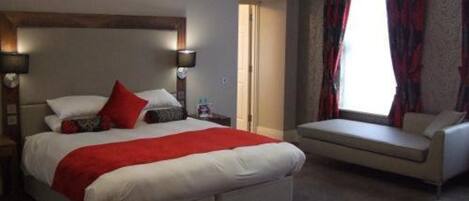 A bedroom with a large bed, bedside lamps, a window with curtains, and a sofa.