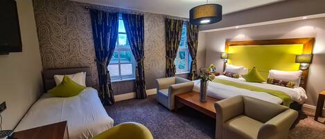A hotel room with two beds, a sofa, a dining table, and a TV.