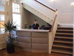 Welcome to our hotel lobby, featuring a central reception desk and a staircase leading to an upper level.