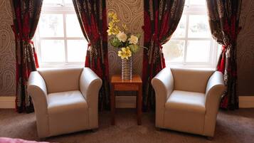 Una habitación con dos sillones color beige, una mesita de madera con un jarrón de flores amarillas y cortinas estampadas.