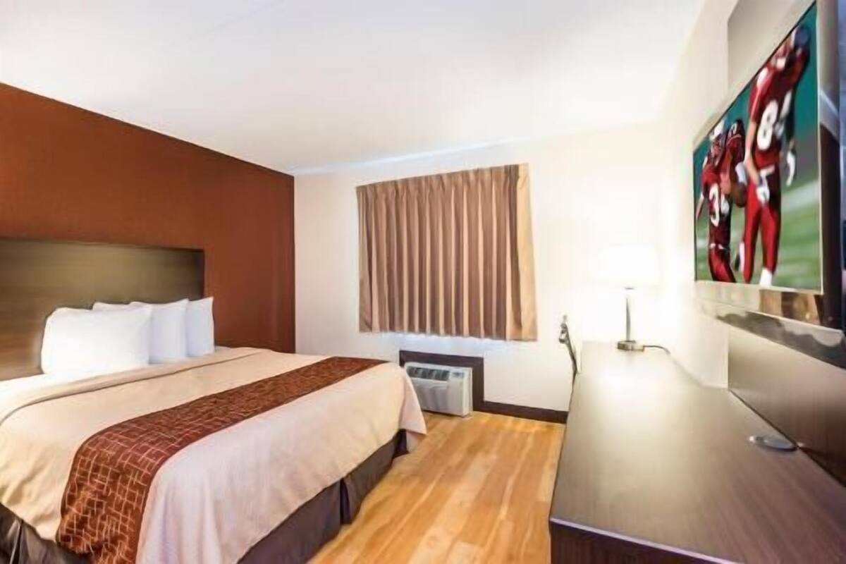 A hotel room with a bed, a desk, a TV, and a window with curtains.