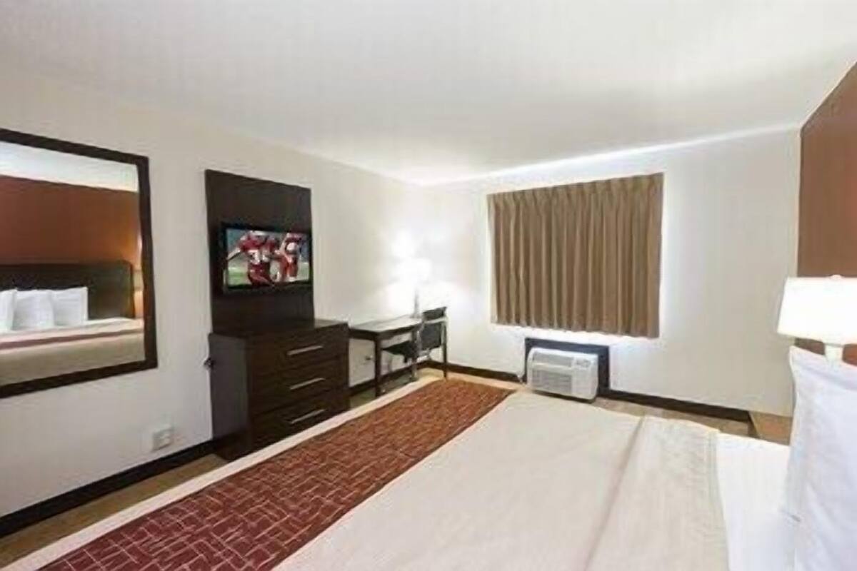 A hotel room with a bed, a TV, a desk, and a window with curtains.