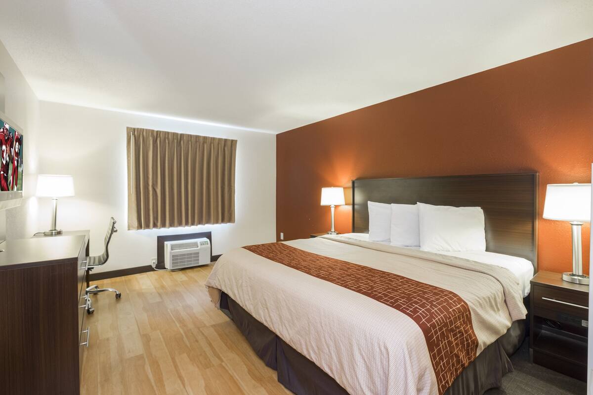A hotel room with a large bed, bedside lamps, a desk with a lamp, a chair, and a window with curtains.