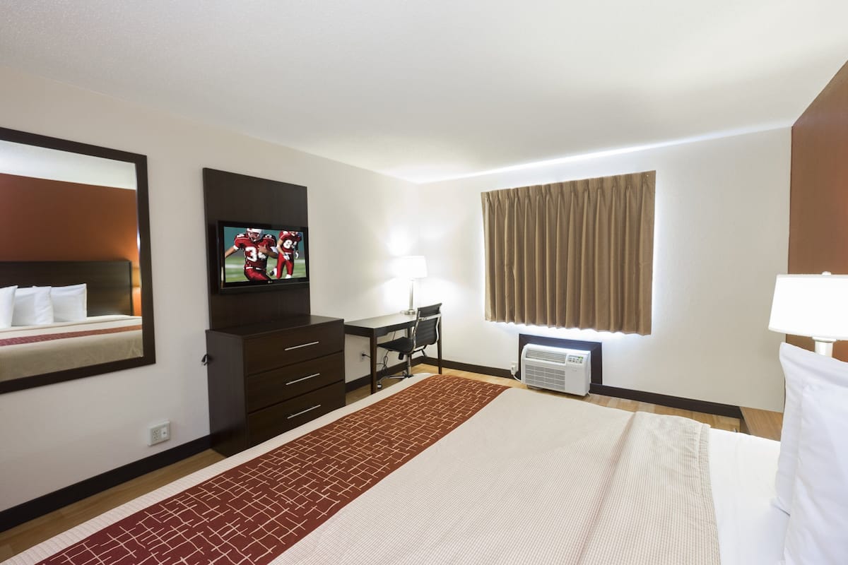 A hotel room with a bed, a desk, a TV, a lamp, and a window with curtains.
