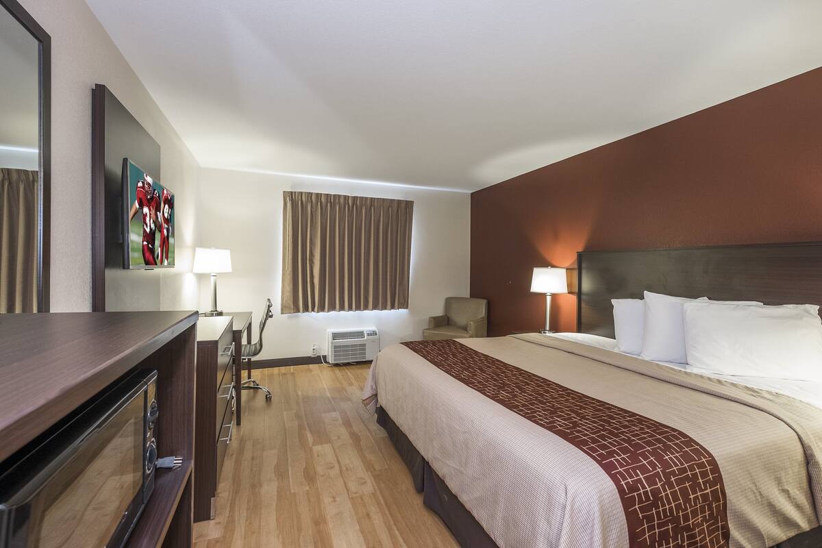 A hotel room with a bed, a desk, a chair, a TV, and a window with curtains.
