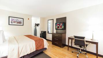 A hotel room with a bed, a desk, a chair, a television, and a small refrigerator.