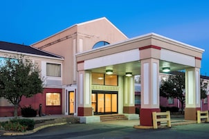 Hotel com entrada coberta, balcão de recepção visível e céu claro.