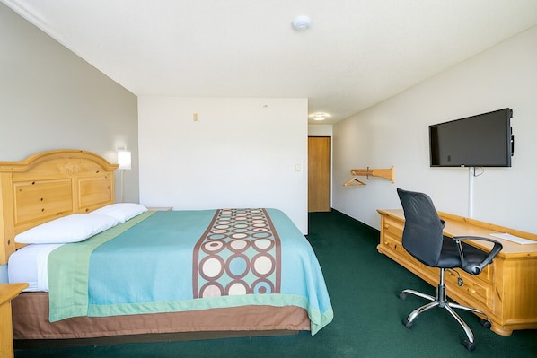 A hotel room with a bed, a desk, a chair, a TV, and a coat rack.