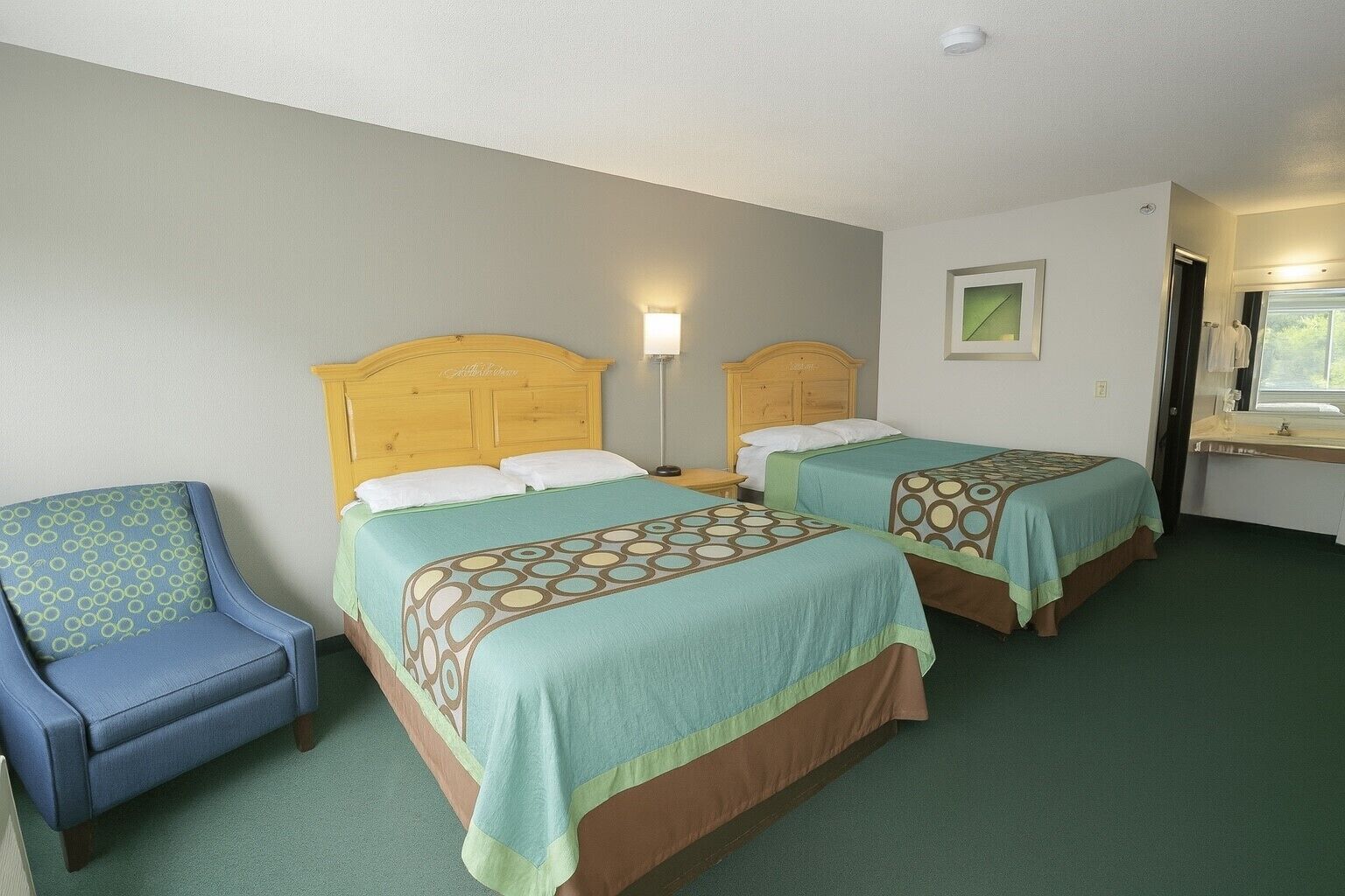 Una habitación de hotel con dos camas, una silla y un ventanal.