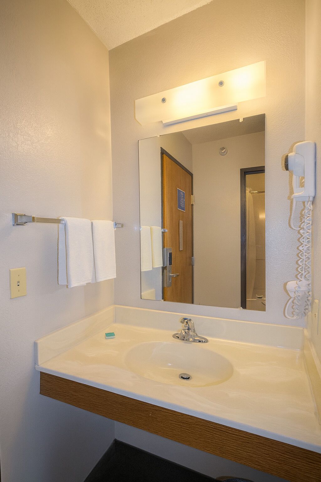 A bathroom with a white sink, a mirror, a towel rack, and a hairdryer on the wall.