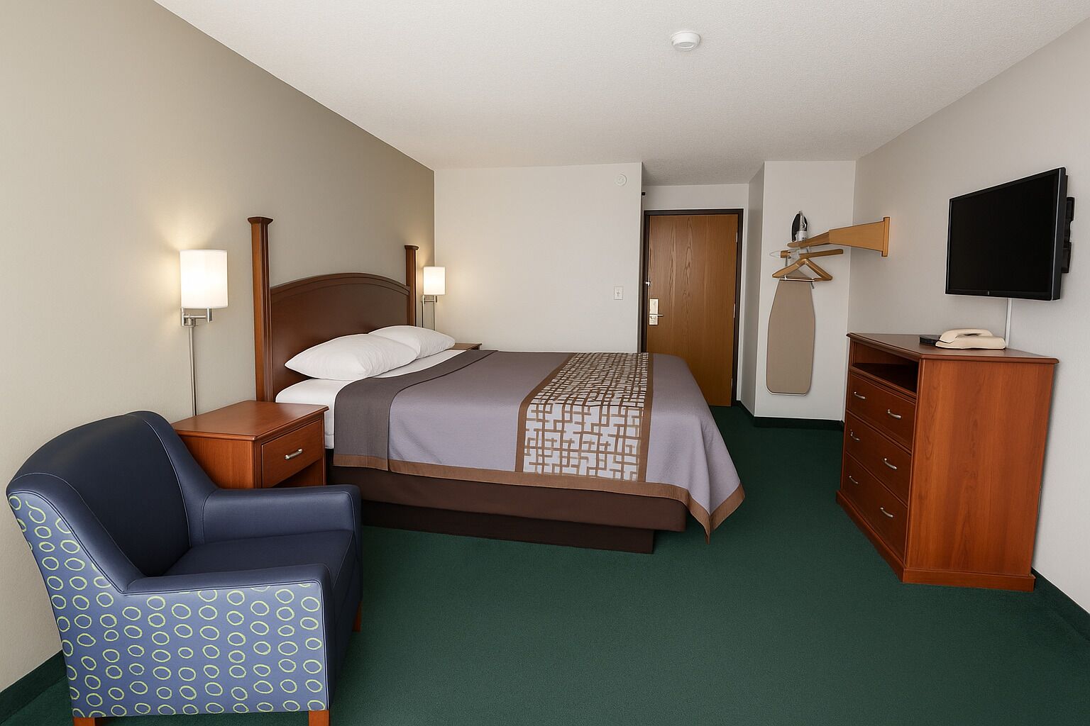 A hotel room with a bed, a desk, a chair, a dresser, and a TV mounted on the wall.