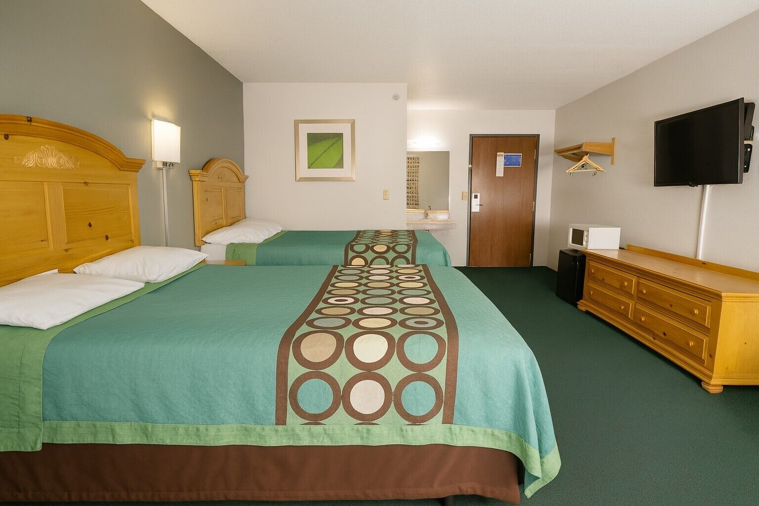 Une chambre d’hôtel avec deux lits, une commode en bois, un téléviseur et une porte avec une pancarte.