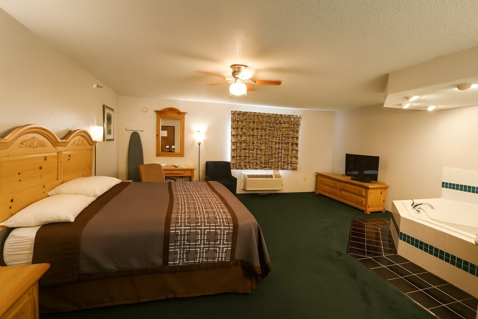 Une chambre d’hôtel comprenant un lit, un bureau, une chaise, une télévision, une salle de bain avec baignoire et un ventilateur de plafond.