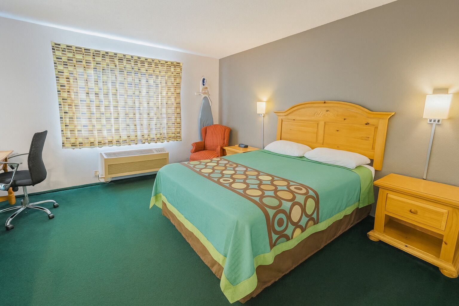 A hotel room with a bed, a chair, a desk, and a window with blinds.