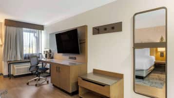 A hotel room with a desk, chair, television, and a bed.