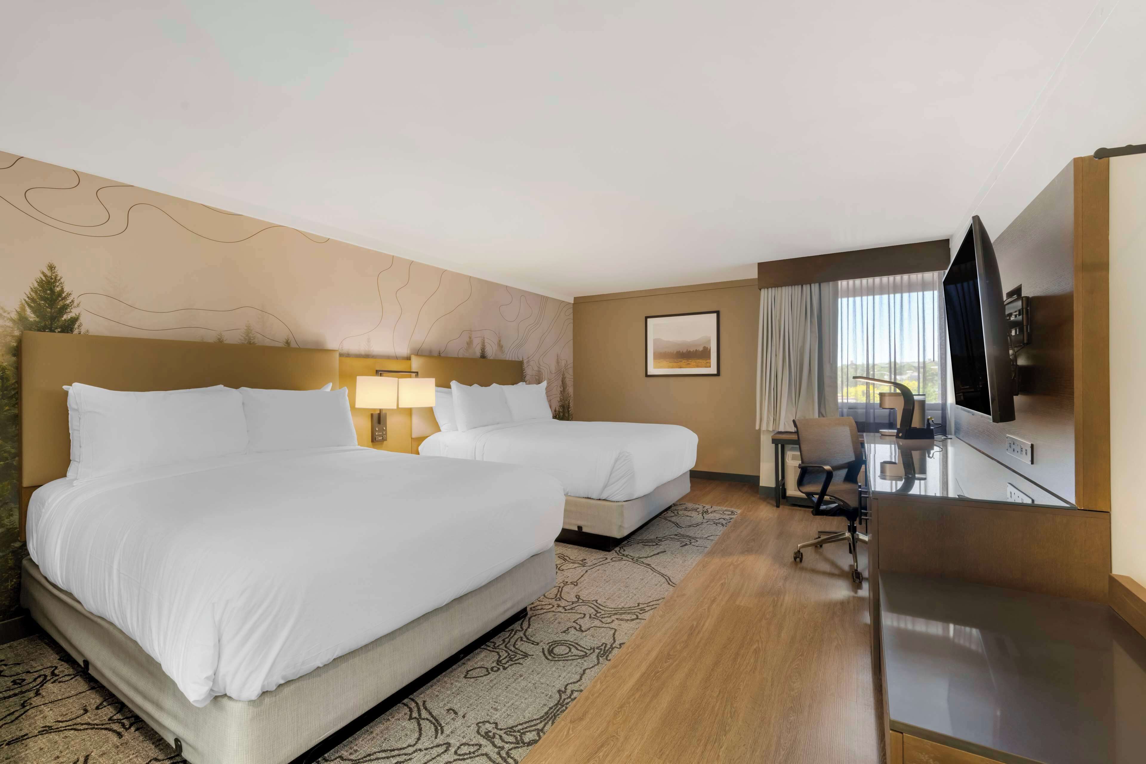 Une chambre d’hôtel avec deux lits, un bureau avec une chaise, une télévision et une fenêtre avec des rideaux.