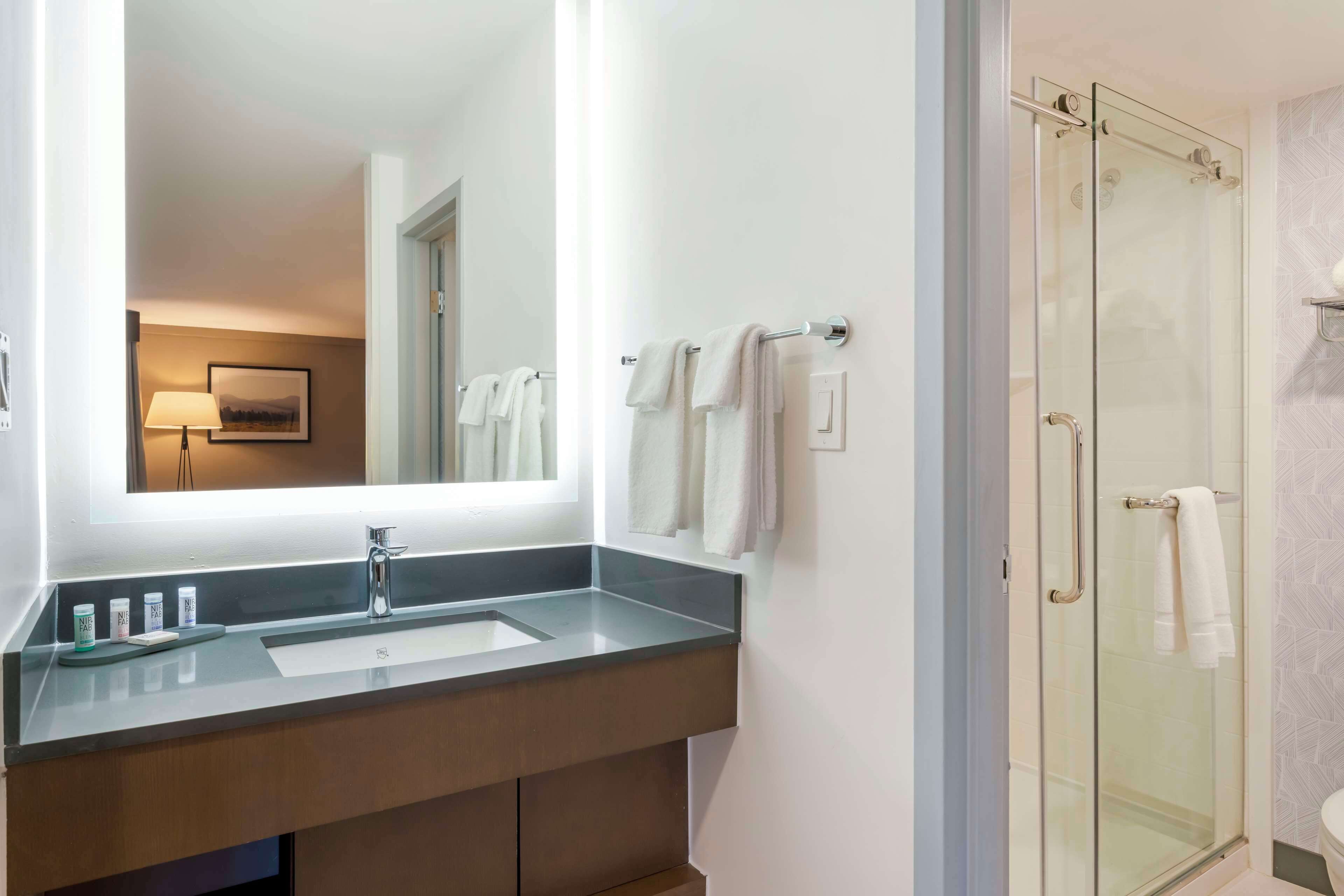 Un baño con cabina de ducha de vidrio, un espejo grande y un lavamanos moderno con un perchero para toallas.