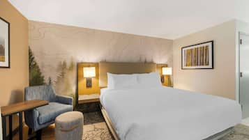 A hotel room with a large bed, a chair, a small ottoman, and a nightstand with lamps.