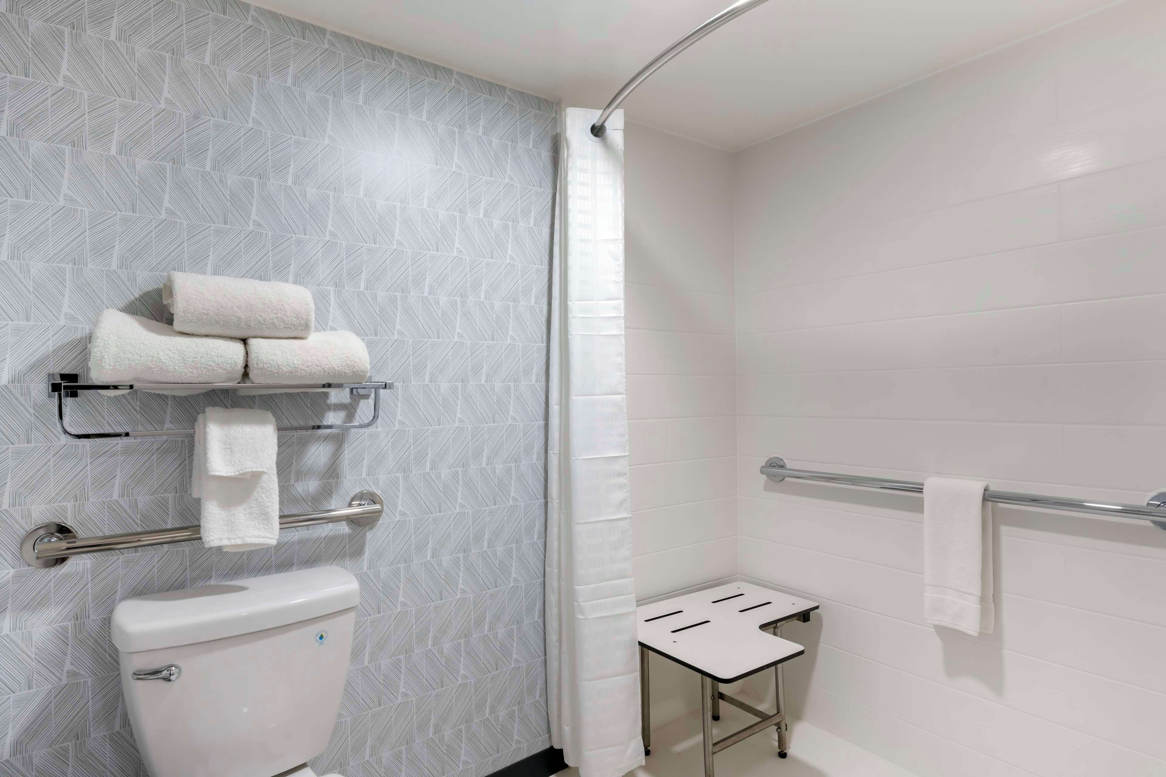 A bathroom with a toilet, a towel rack, a shower curtain, and a small table.