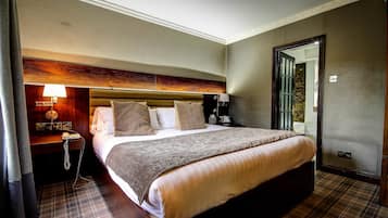 A hotel room with a large bed, a bedside table with a lamp, a wooden headboard, and a door leading to a balcony.