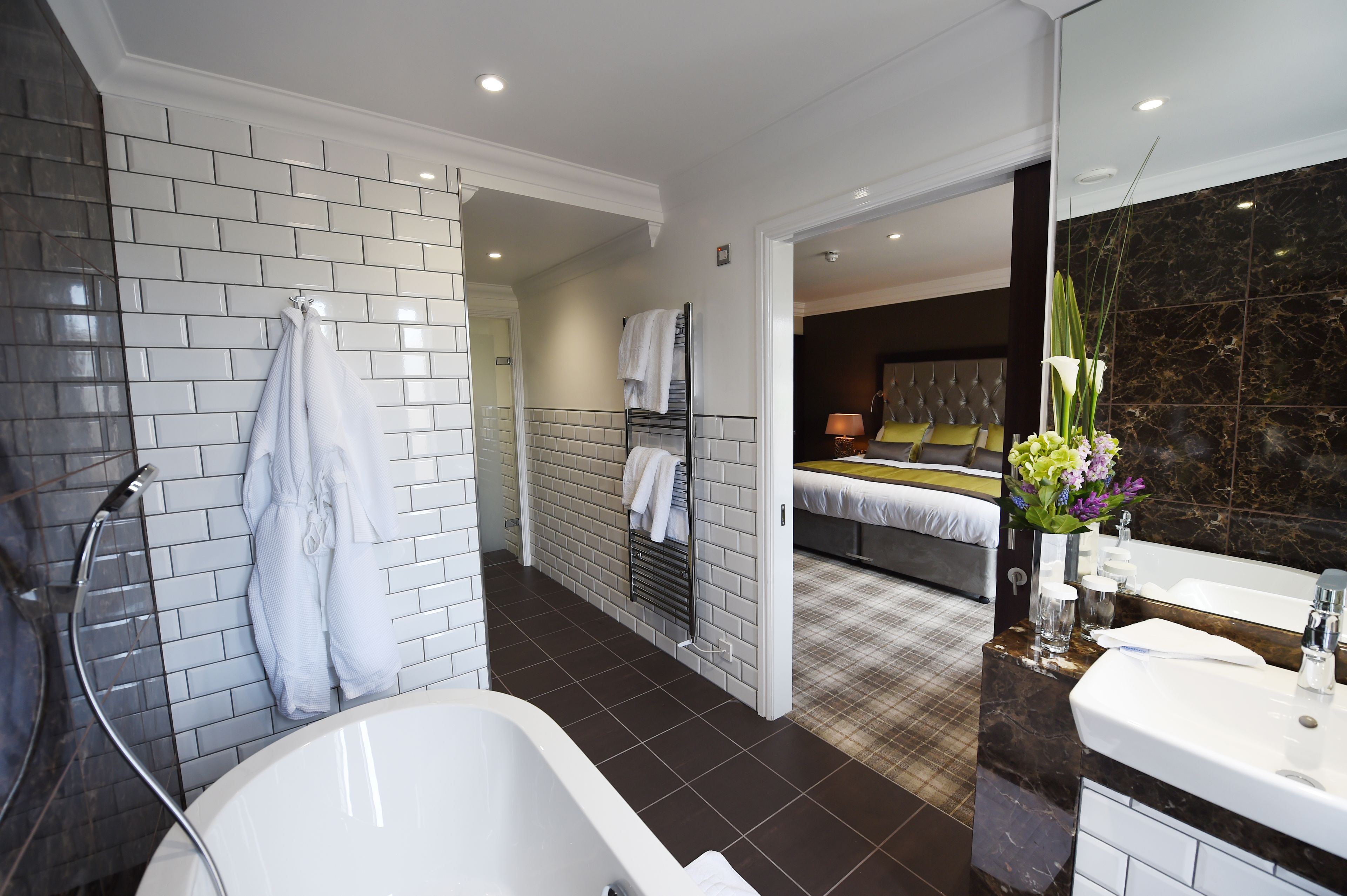 A modern bathroom with a bathtub, a shower, and a toilet. There is a bed visible in the background.