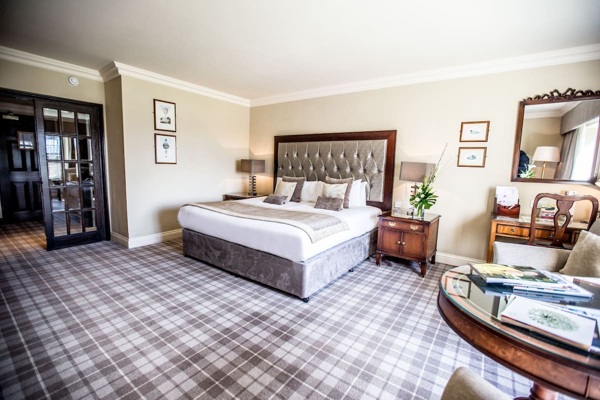 A hotel room with a large bed, a bedside table with a lamp, a mirror, and a checkered floor.