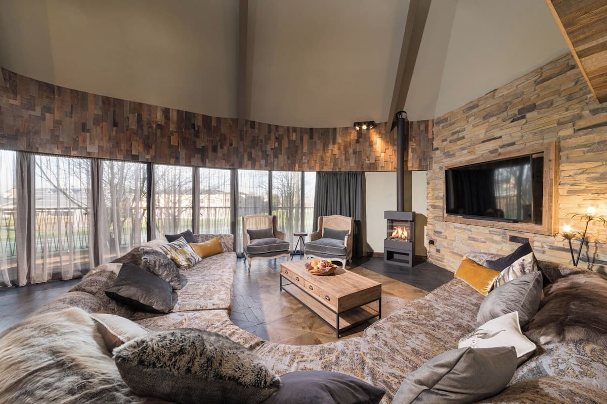 A spacious living room with a large sectional sofa, two armchairs, a wooden coffee table, and a stone fireplace.