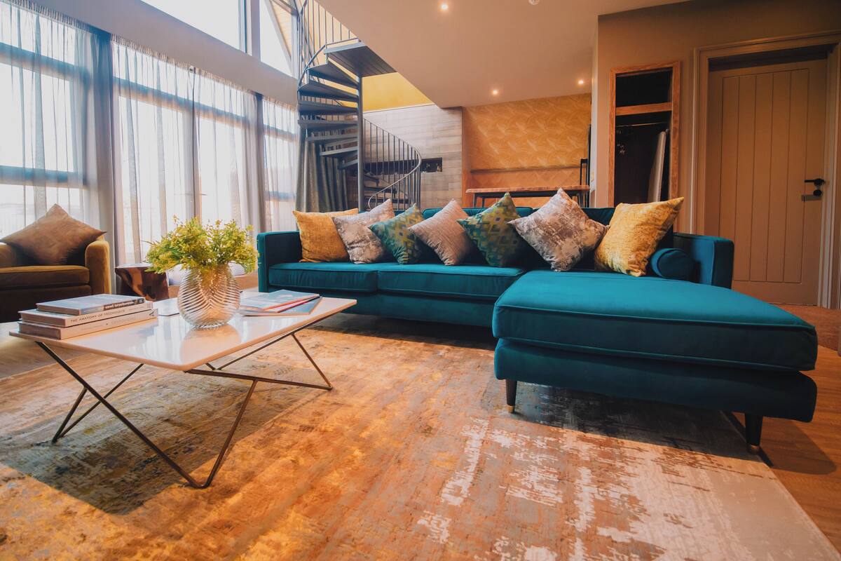 A modern living room with a teal sofa, a white coffee table, and a spiral staircase in the background.