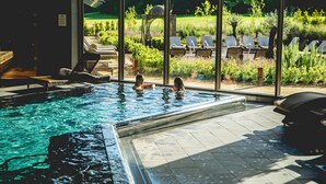 A swimming pool with two people in the water, surrounded by lounge chairs and a view of a garden. - Ramside Hall Hotel, Golf and Spa (Durham)