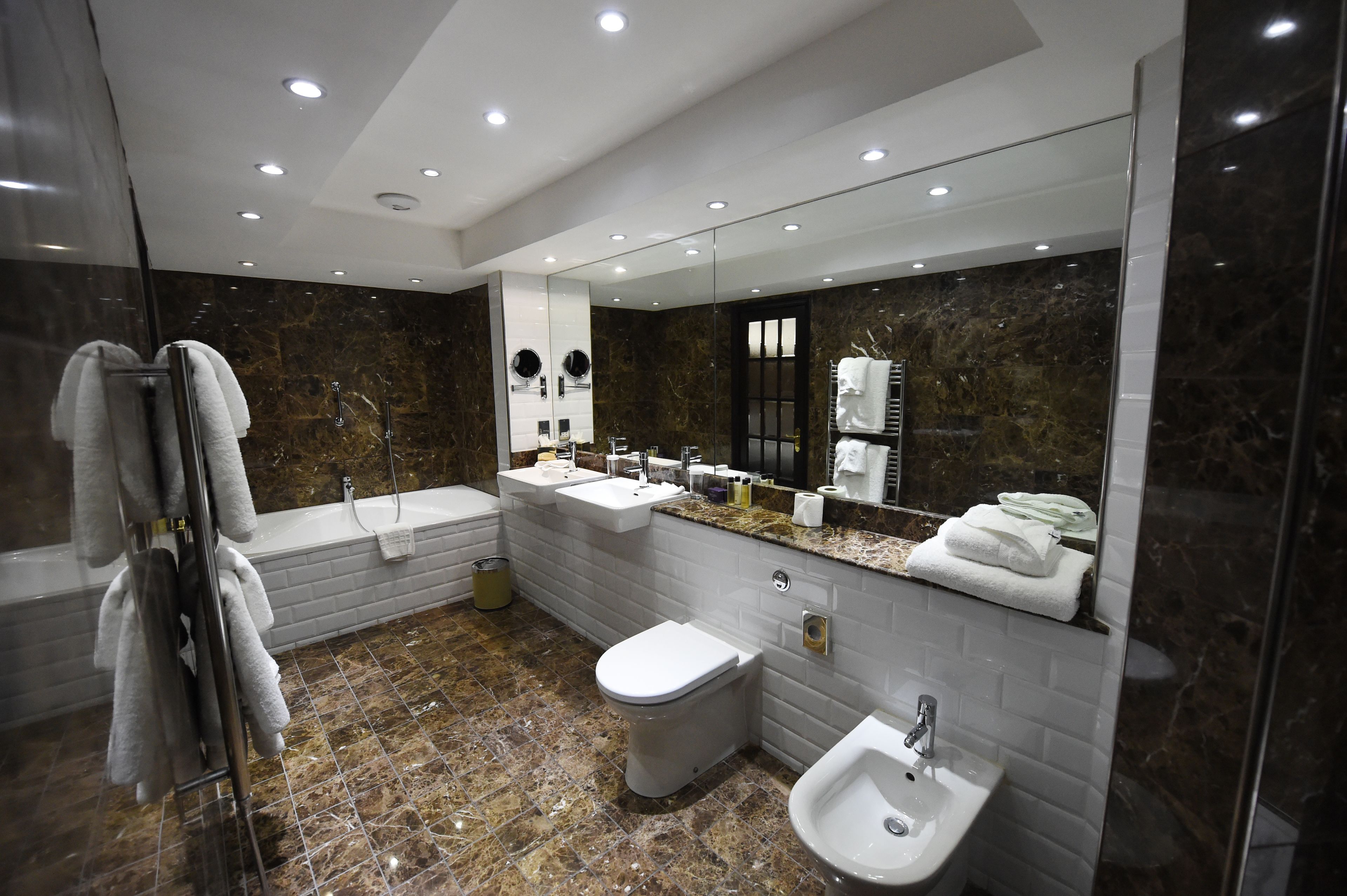 Ein modernes Badezimmer mit Marmorboden, einem großen Spiegel, einer Badewanne, einer Toilette und einem Waschbecken.