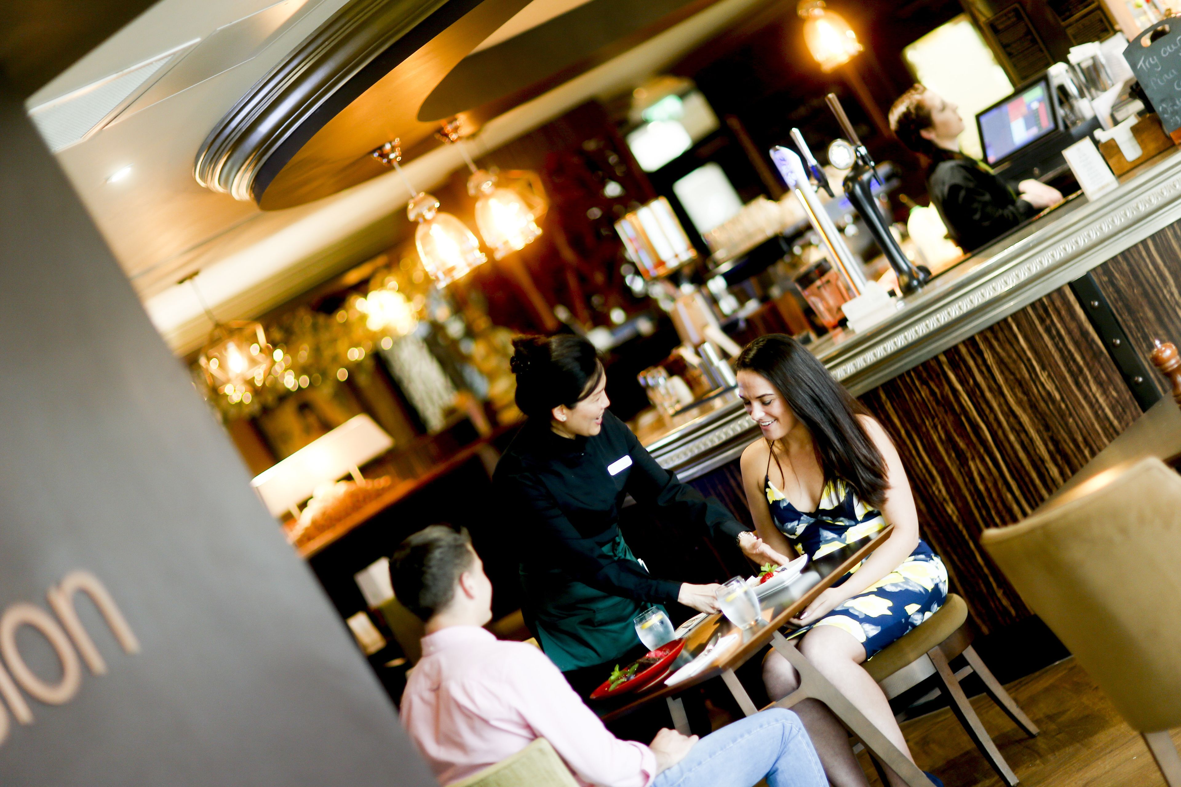 A restaurant interior with a bar area, tables, and hanging lights.