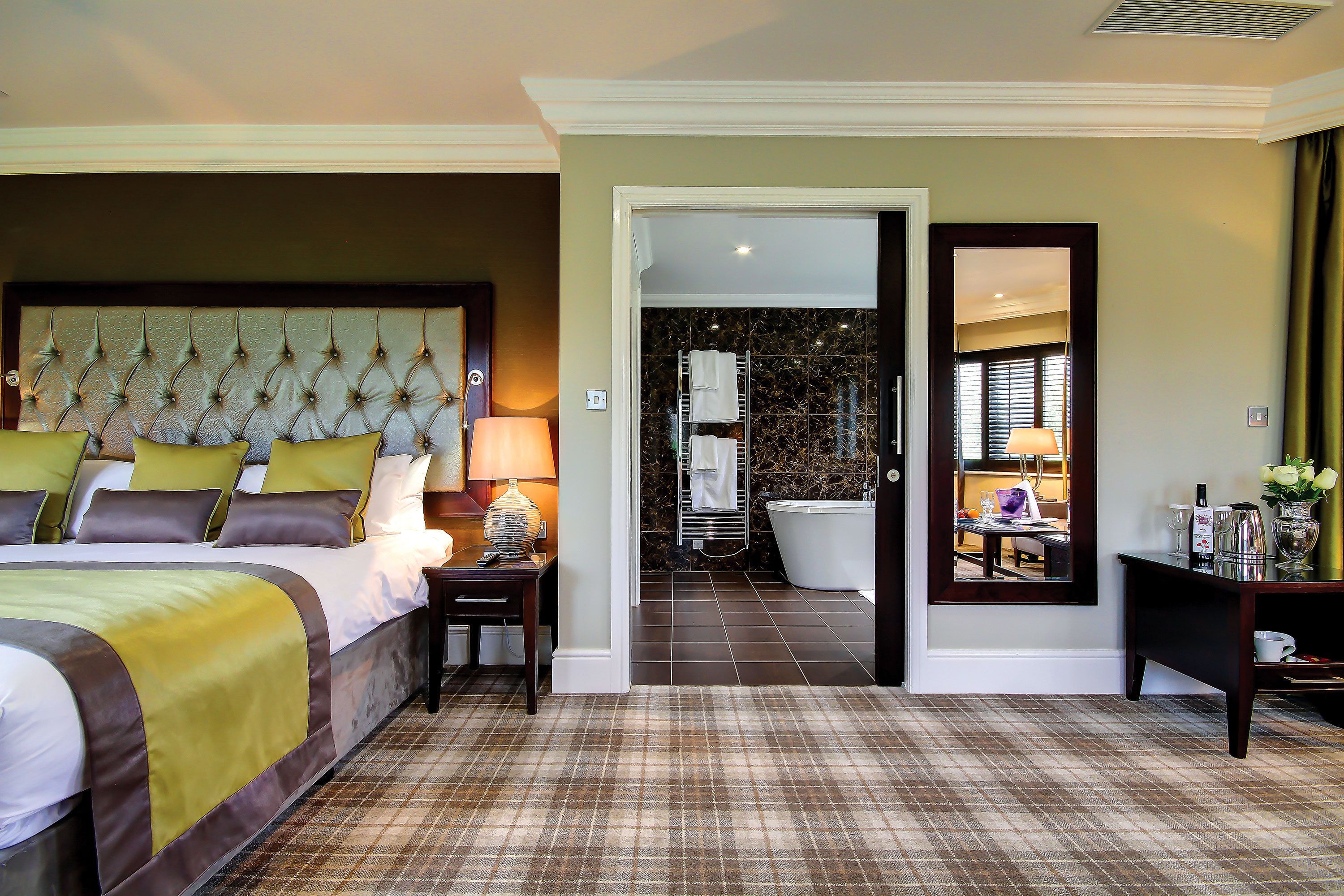 A hotel room with a large bed, a bathroom with a bathtub, and a mirror reflecting the bathroom.