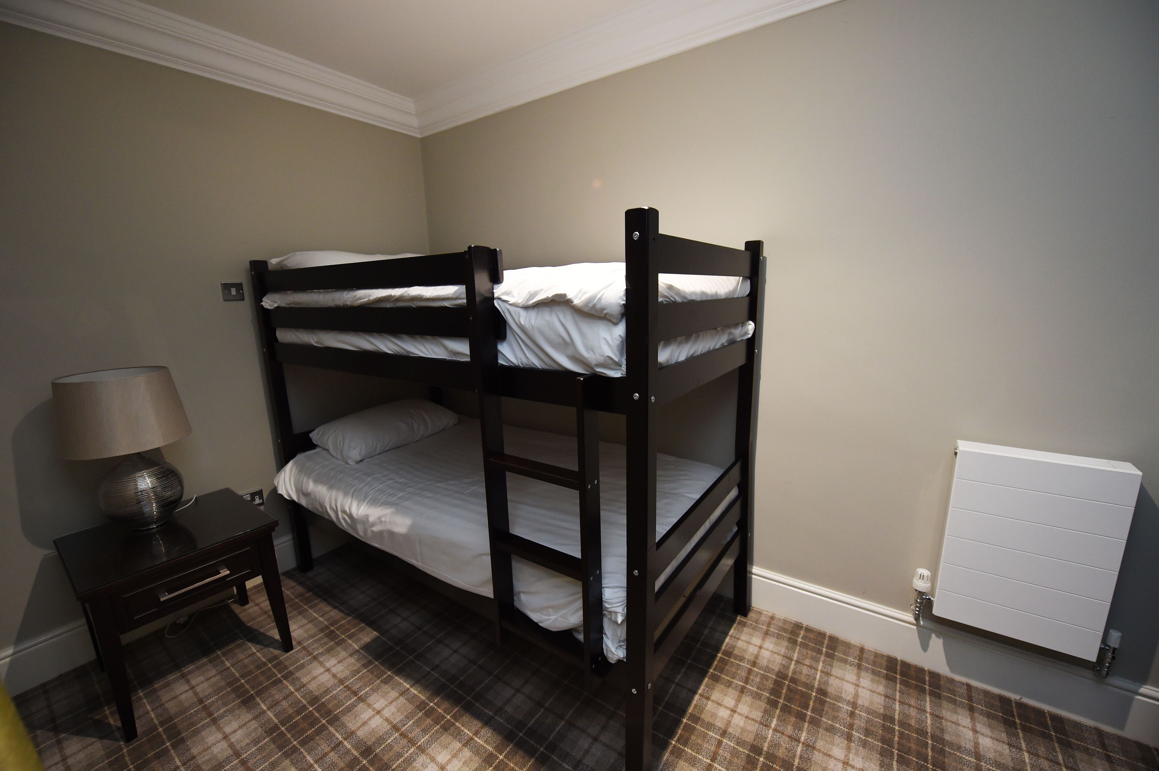 A bunk bed room with a nightstand, a lamp, and a radiator.