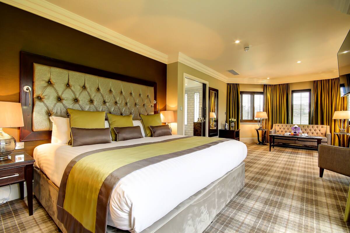 A spacious hotel room with a large bed, a sofa, and a desk.