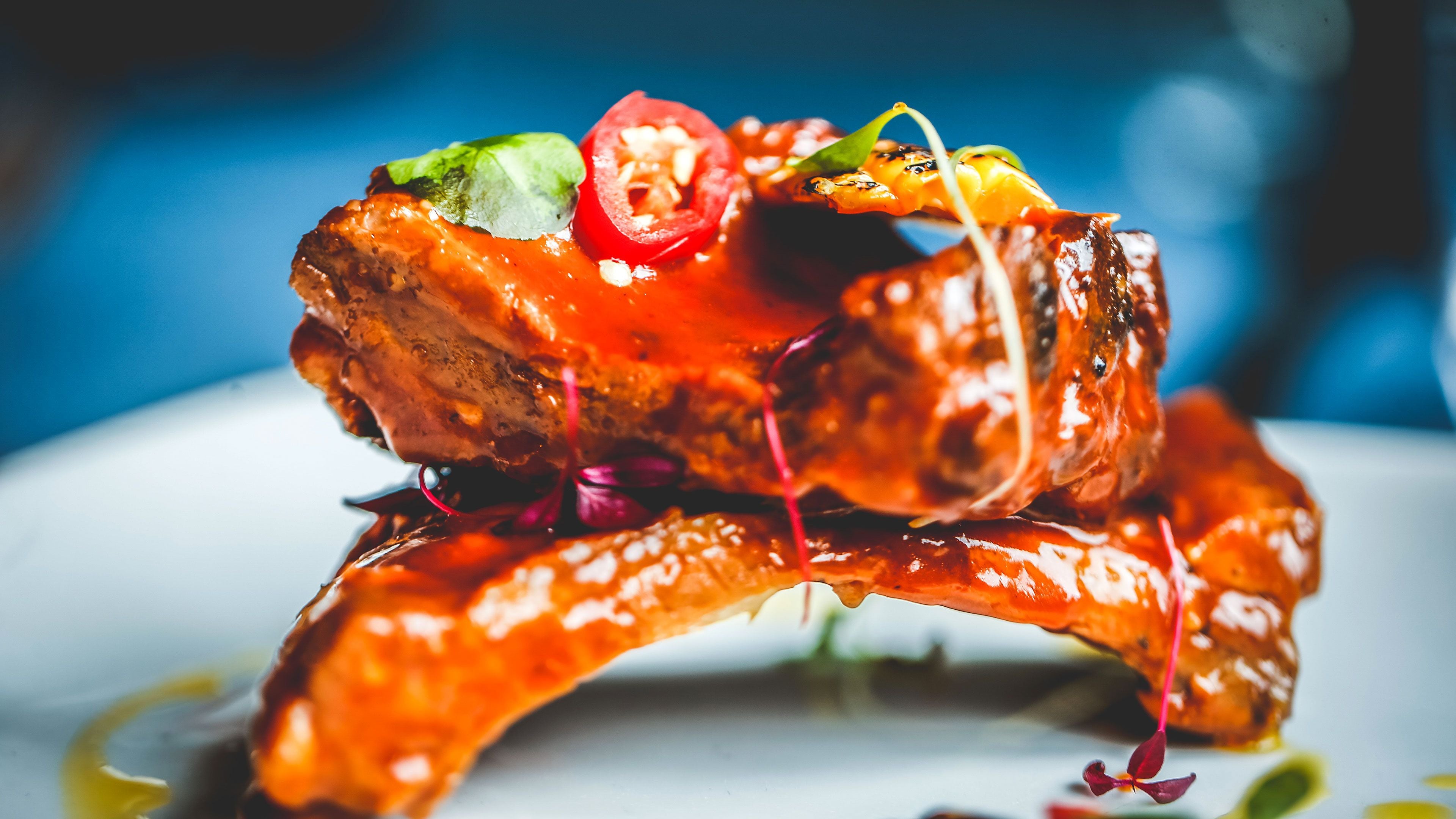 A dish with a glazed meat centerpiece, garnished with red pepper and green leaves.