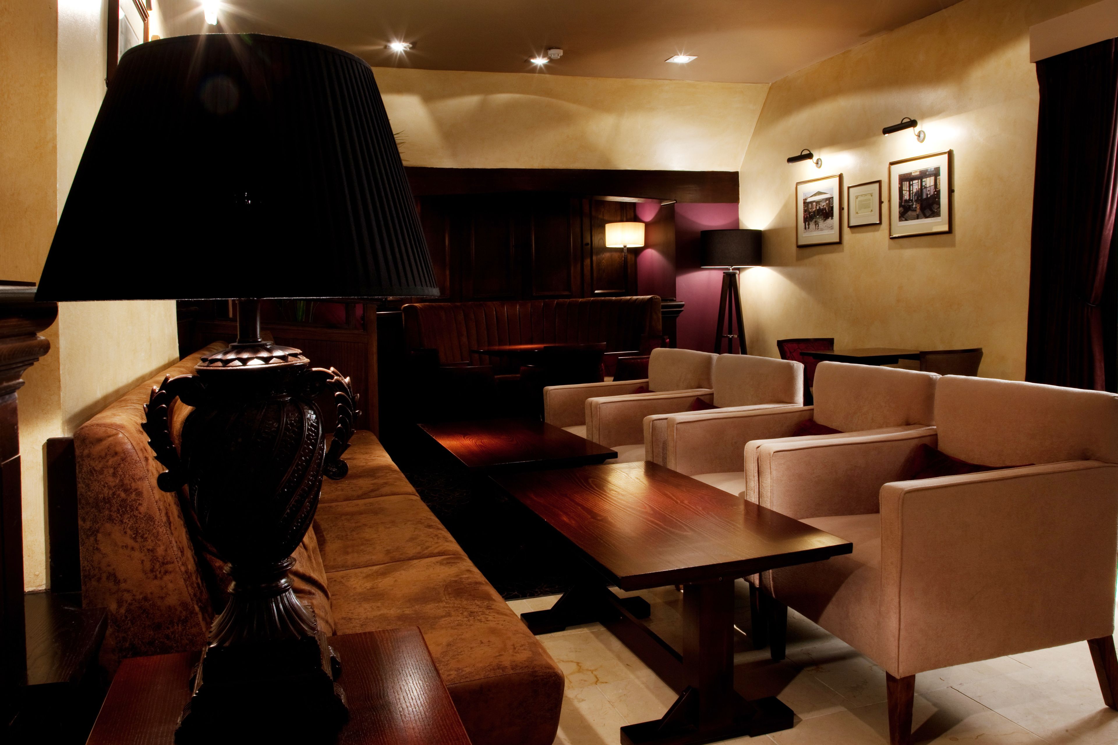 Un hall d’entrée avec une longue table en bois, plusieurs fauteuils, une lampe sombre et des tableaux encadrés accrochés au mur.