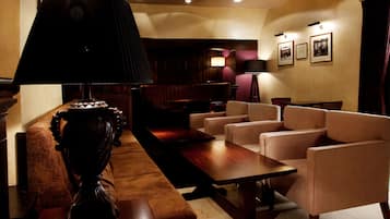 Un hall d’entrée avec une longue table en bois, plusieurs fauteuils, une lampe sombre et des tableaux encadrés accrochés au mur.