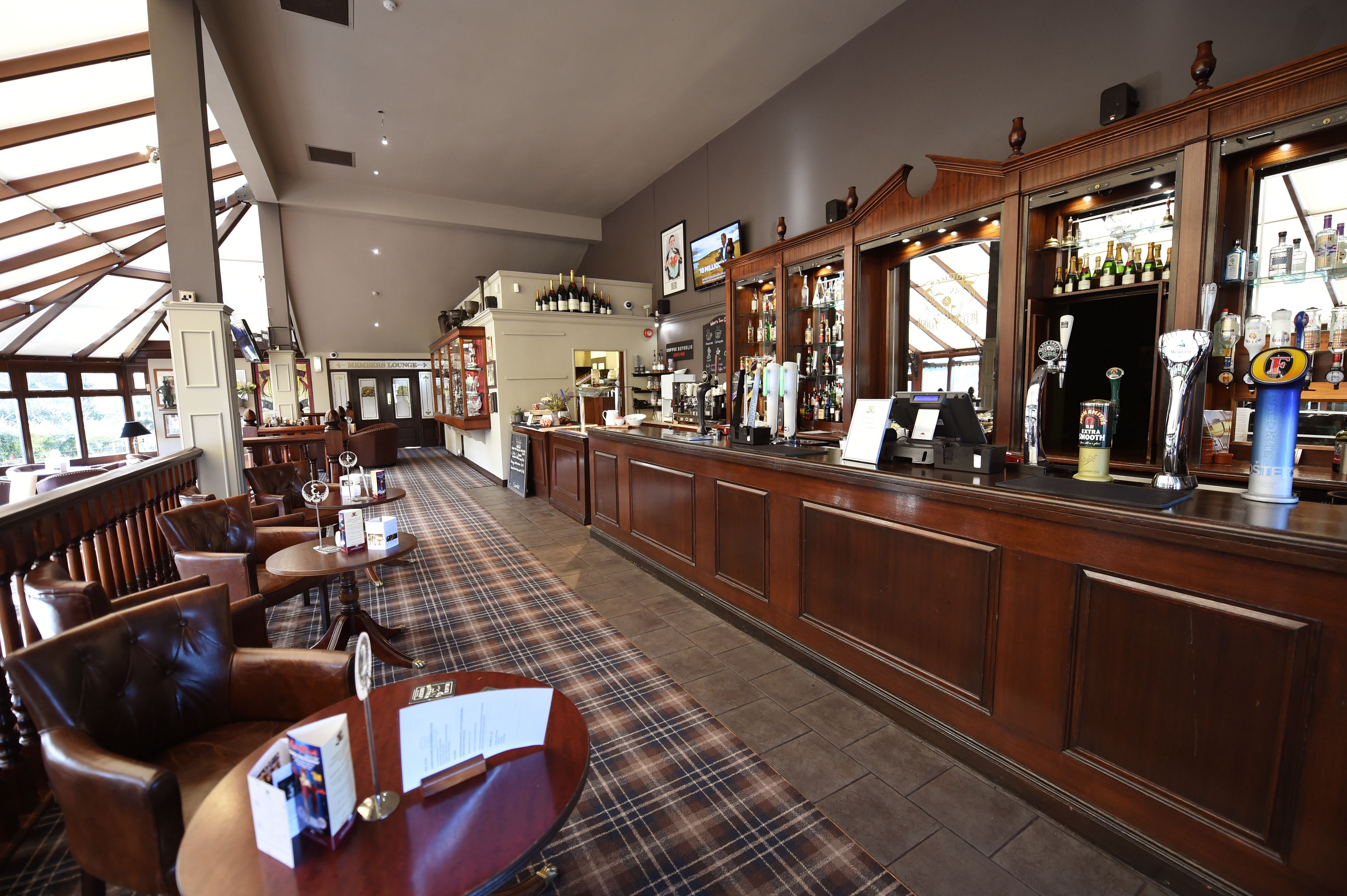 A bar area with wooden furniture, a bar counter, and a variety of bottles and glasses.