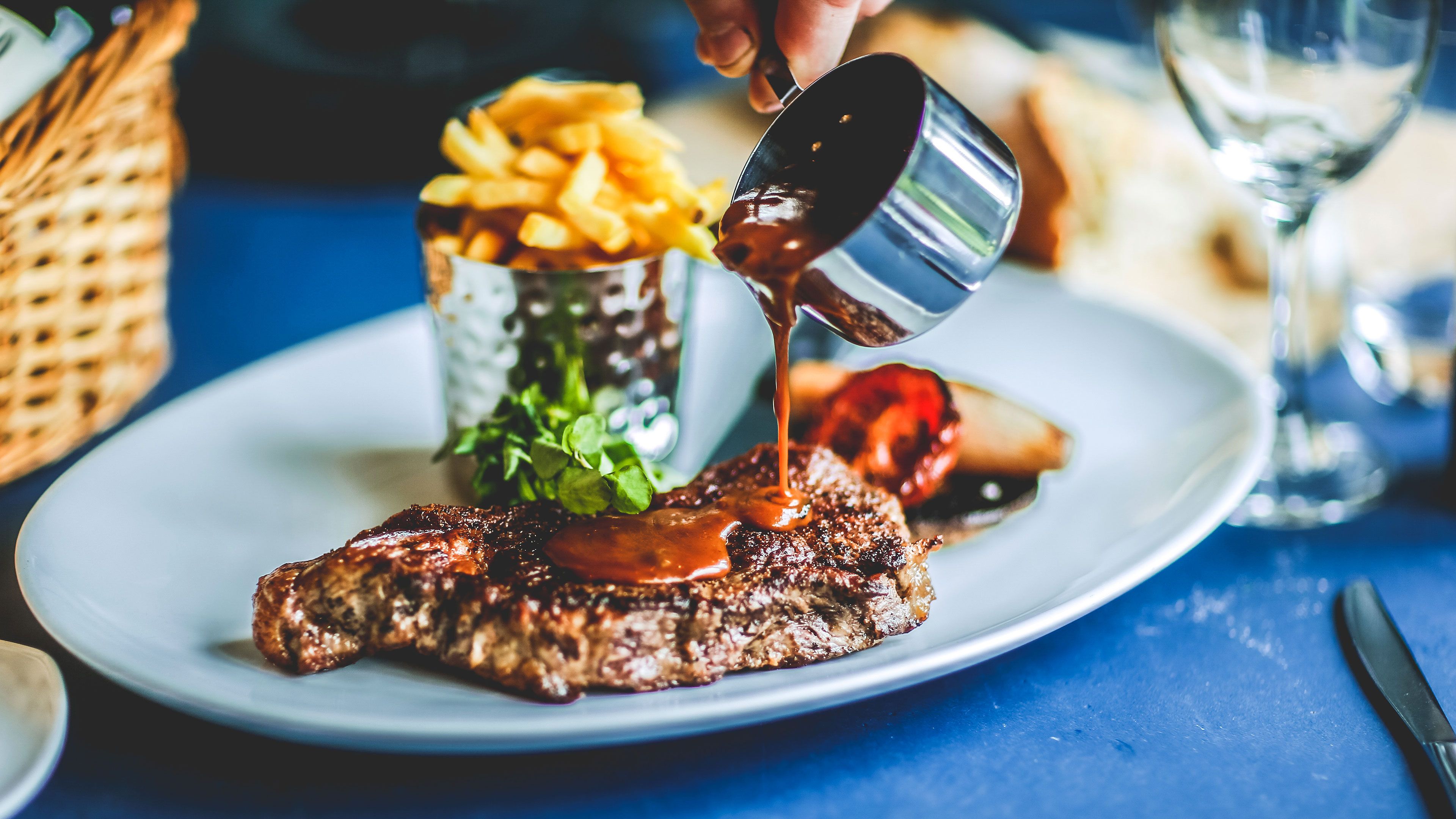A steak with sauce on a plate, accompanied by a side of fries and a glass of water.