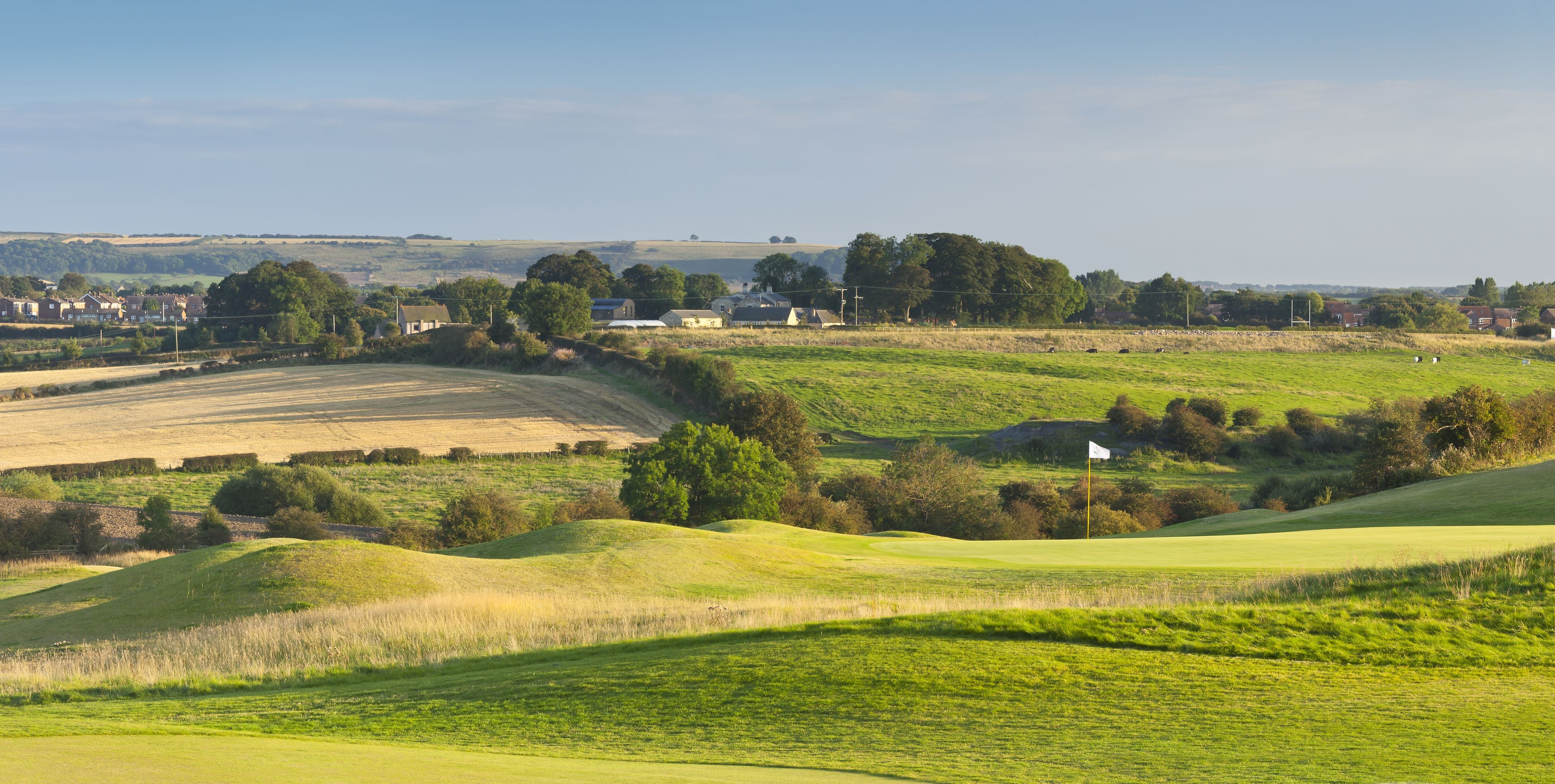 A rural landscape with rolling hills, a golf course, and scattered houses.