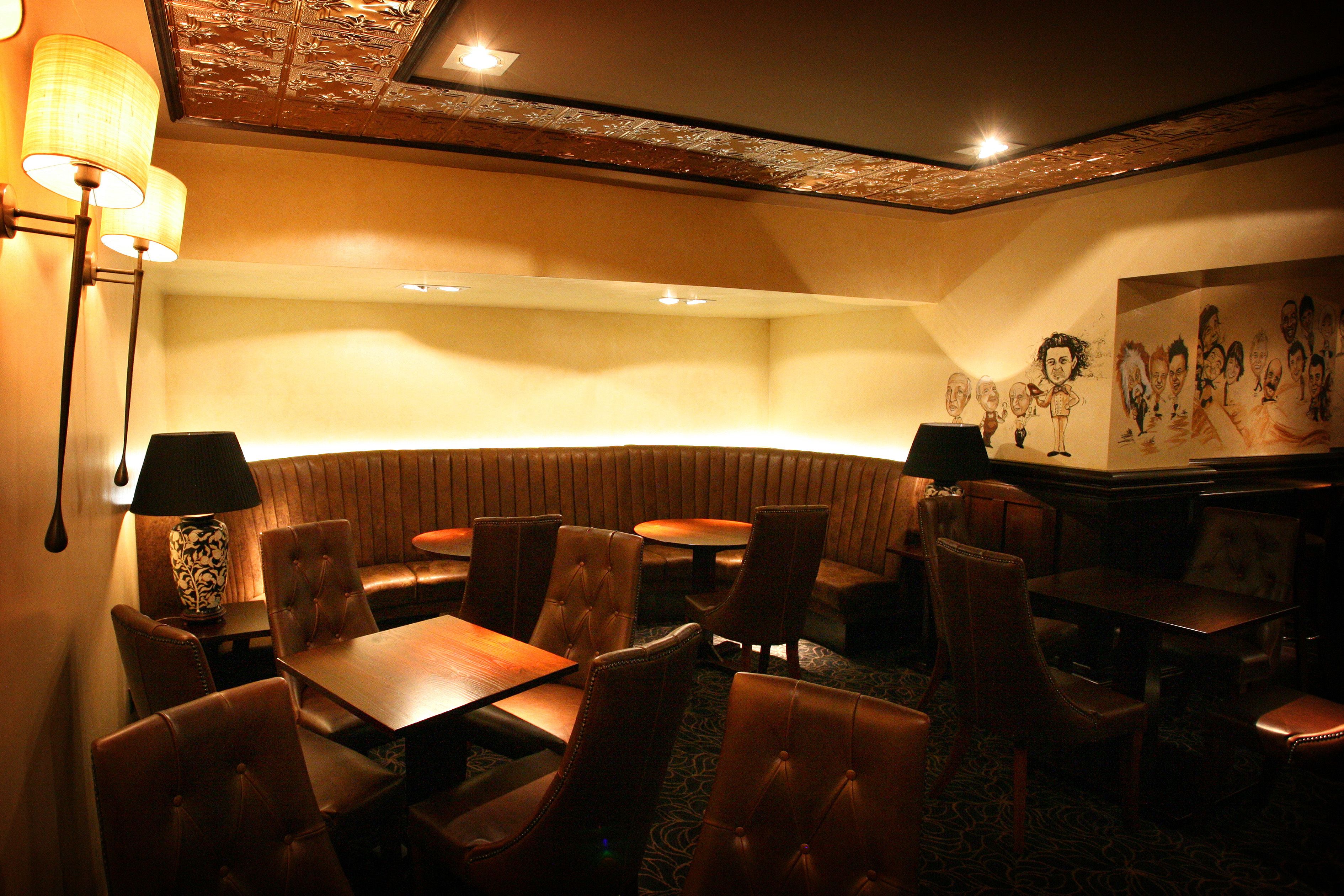 A dimly lit restaurant with booths and tables, a patterned ceiling, and wall art.