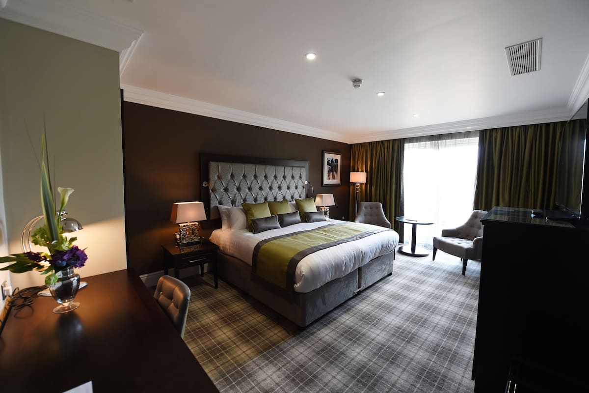 A hotel room with a large bed, a desk, a chair, a TV, and a window with curtains.