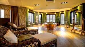 A room with wicker furniture, a large bathtub, and a mirror. - Ramside Hall Hotel, Golf and Spa (Durham)