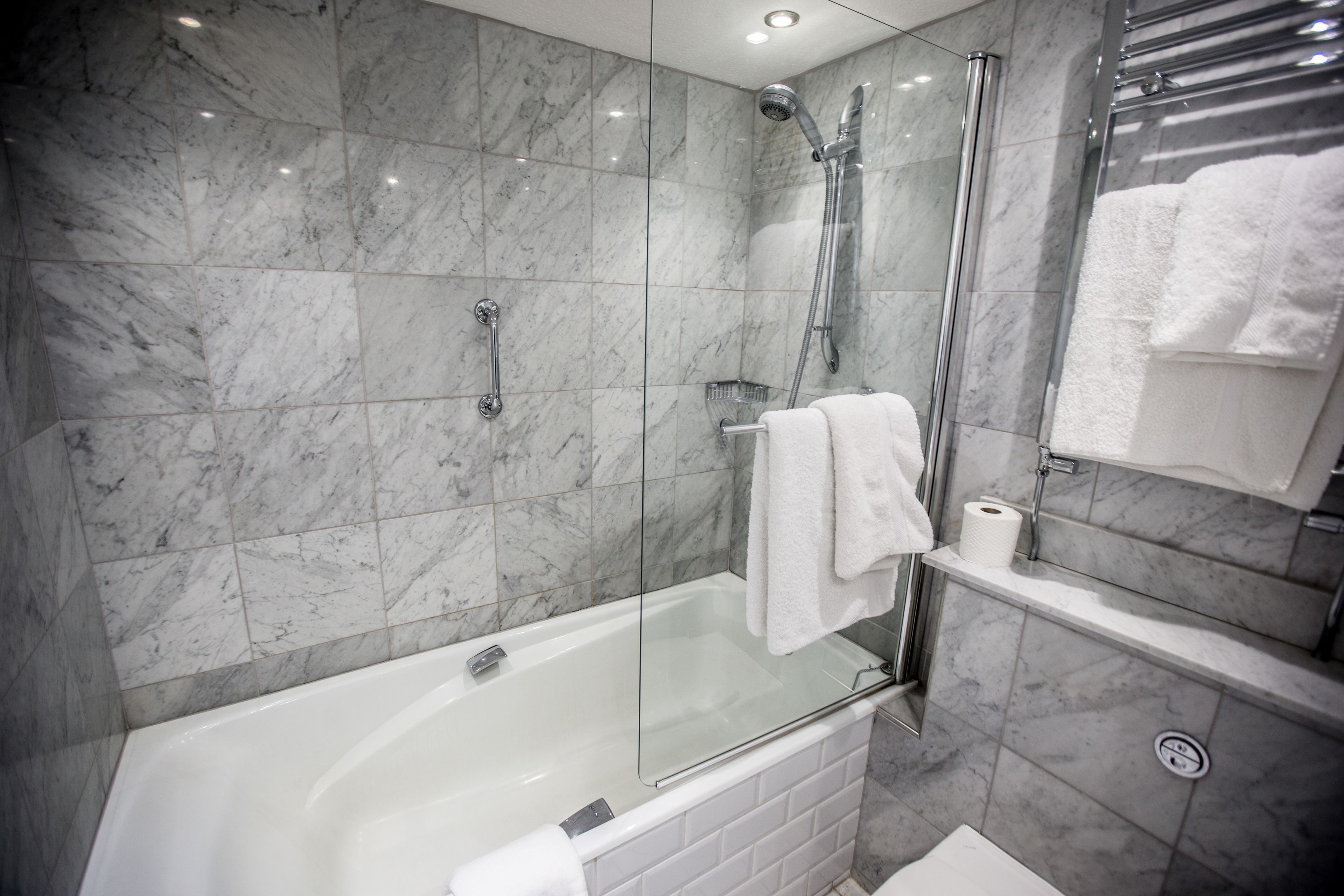 A modern bathroom with a glass-enclosed shower, a white bathtub, and a marble-tiled wall.